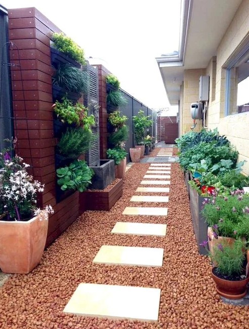 a stylish and bright side yard with pebbles and pavements, potted greenery and blooms and a vertical garden