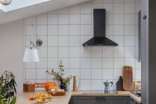 62 a small attic kitchen with graphite grey lower cabinets, a white square tile backsplash, a black hood and greenery