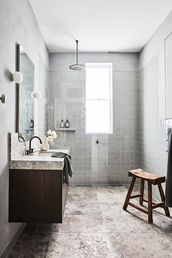 a wabi-sabi bathroom with grey square tiles and large format stone tiles, a floating vanity, a stained wooden stool and a mirror