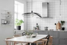 64 a stylish Scandinavian kitchen with white square tiles, grey shaker cabinets, a hood, a white table and stained chairs and a catchy pendant lamp