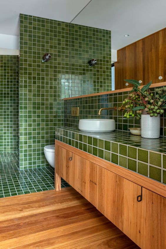 a welcoming bathroom with green square tiles and a stained floor and vanity, white applinaces and brass fixtures and a large mirror