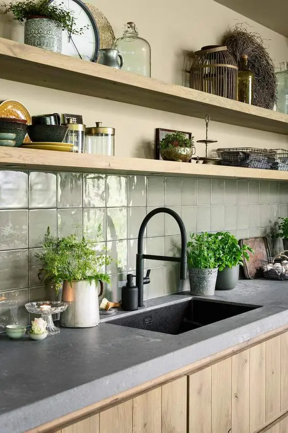 a stylish stained kitchen with a grey stone countertop, a light green square tile backsplash and open shelves is wow