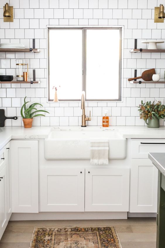 a white farmhouse kitchen with shaker cabinets, a white square tile backsplash, white countertops, open shelves and potted plants
