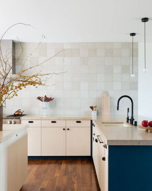 An eye catchy modern kitchen with navy and stained lower cabinets, a grey square tile backsplash, stone countertops, black fixtures