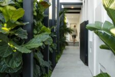 74 an ultra-modern side yard with a tiled path, greenery and tropical plants and some black wooden beams over the path