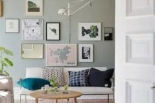 a Nordic living room with a pale green accent wall, a creamy loveseat, a gallery wall, a sconce, a round table and neutral rugs
