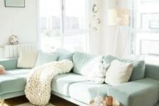 a Scandinavian living room with a mint green sectional, neutral and mint pillows, a knit blanket, a side table and a floor lamp