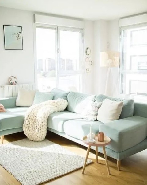 a Scandinavian living room with a mint green sectional, neutral and mint pillows, a knit blanket, a side table and a floor lamp