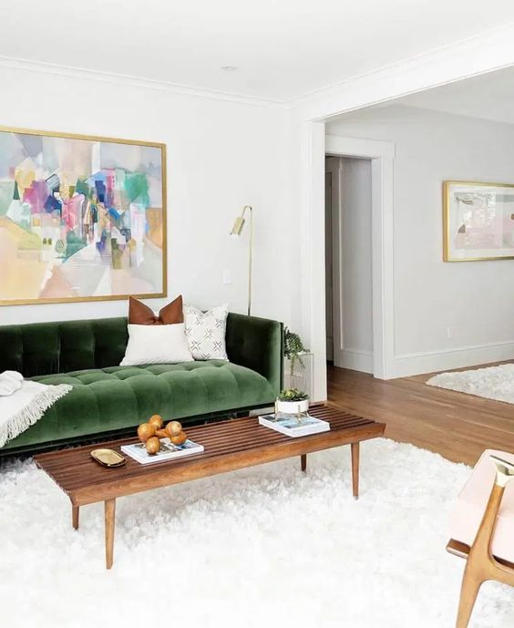 a beautiful living room with a green velvet sofa, a stained coffee table, a neutral chair, a large fluffy rug and a bold artwork