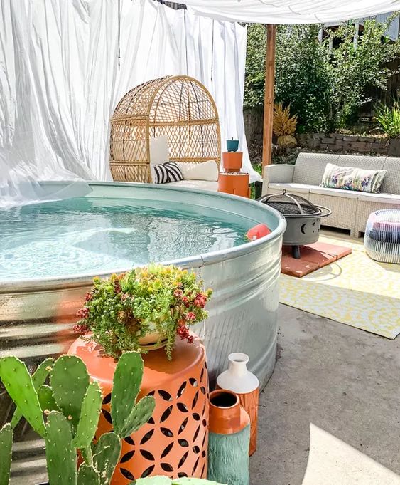 A catchy backyard with a stock tank pool, a sofa, a tent, an egg shaped chair, a grill and some bright decor