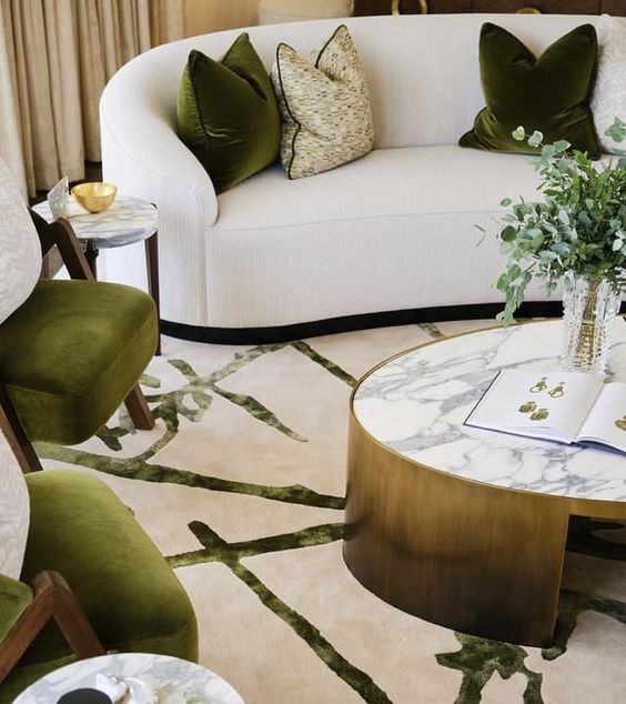 a chic and elegant living room with a curved sofa with green pillows and green chairs, an oval coffee table and a printed rug