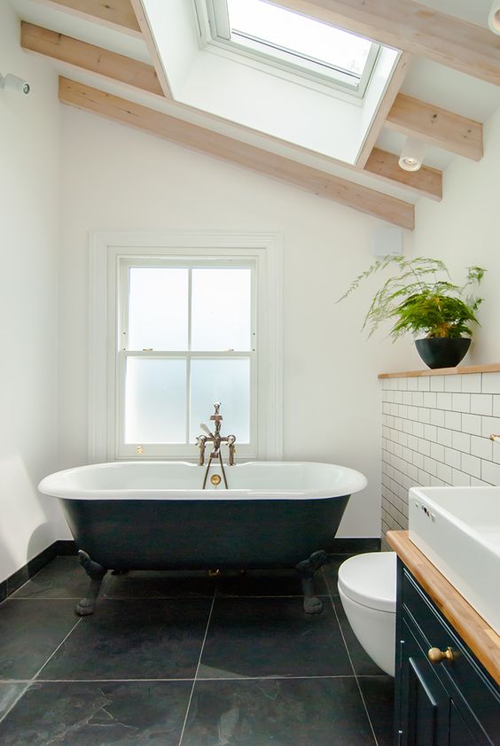 a chic attic bathroom with a window and a skylight, black large scale tiles and white subway ones, a black vanity and a black tub