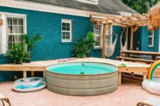a cool and bright backyard with a wooden deck at the stock tank pool, loungers with colorful pillows, potted plants is welcoming