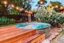 a cool outdoor space with a stock tank pool, some greenery and cacti around, a stepped wooden deck and string lights