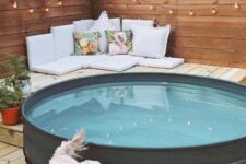 a cool outdoor space with a wooden deck, walls with lights, a stock tank pool, some pillows, cushions and potted plants