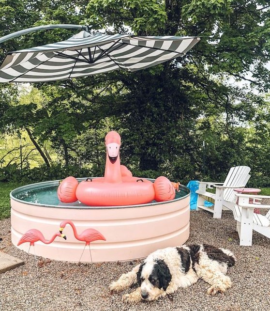 a cool pool space with a stock tank pool in blush, with a flamingo float, flamingos and a striped umbrella and outdoor chairs
