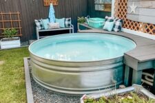 a cozy outdoor space with a stock tank pool, a grey bench, some more benches with pillows and potted plants