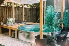a lovely boho nook with a stock tank pool, a wooden bench with pillows, potted plants and gravel around