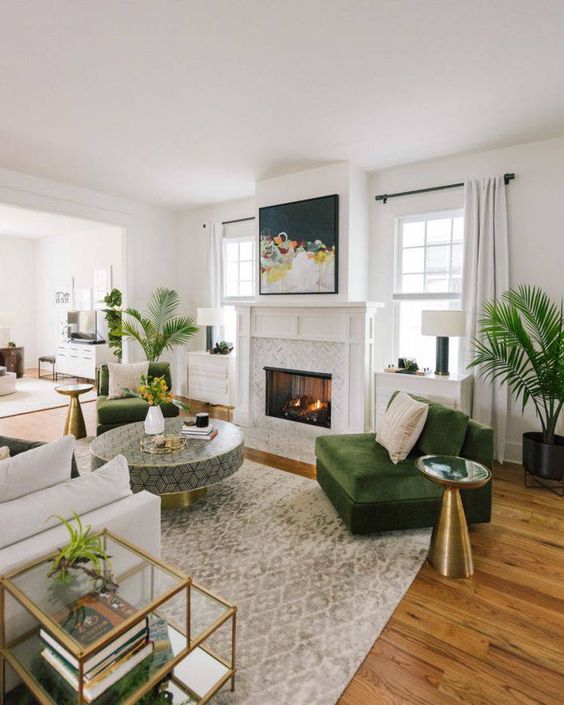a lovely living room done in neutrals, with a fireplace, green chairs, a round geometric coffee table, a neutral sofa and coffee tables plus greenery