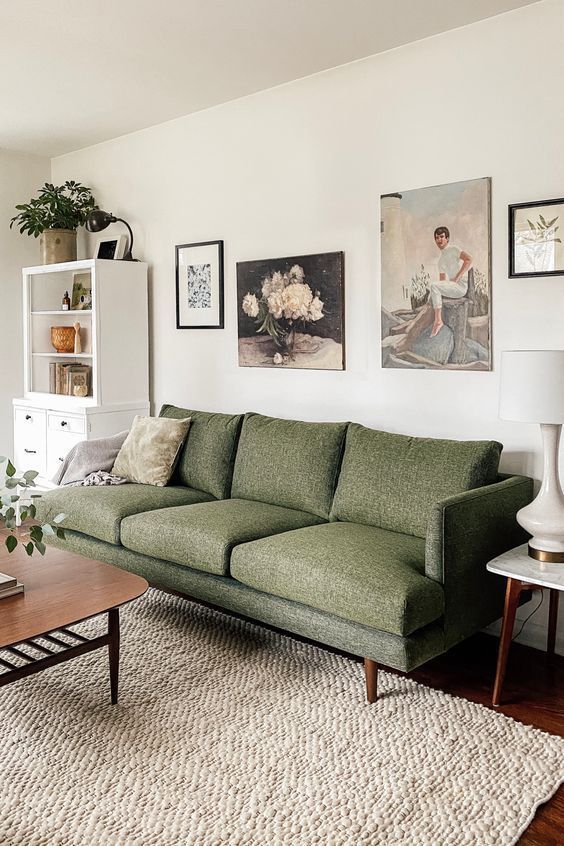 a lovely living room with a green sofa, a white storage unit, a coffee table, a stained table, a large rug and a creative gallery wall