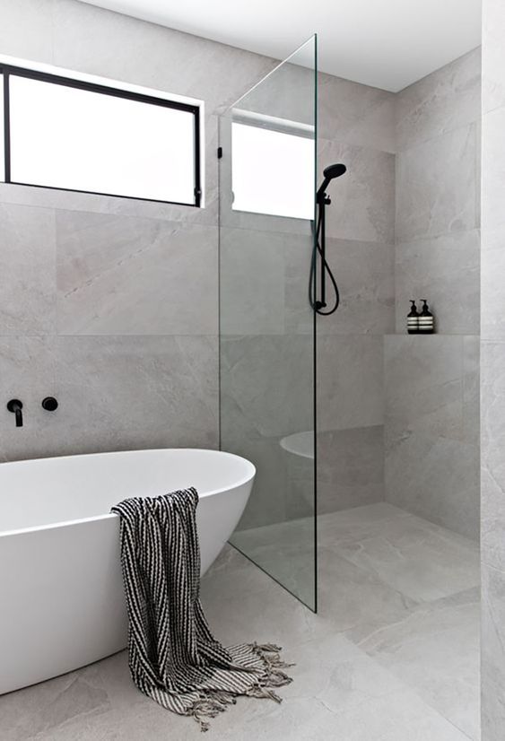 a minimalist bathroom with grey stone large scale tiles, an oval tub and a shower space plus a window