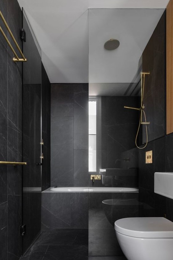 a minimalist black and gold bathroom with black marble tiles, gold fixtures and white appliances is super stylish