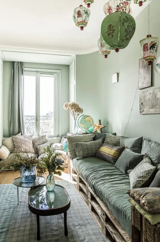 a mint green living room with matching curtains, a green pallet sofa with printed pillows, a couple of coffee tables and Chinese lamps