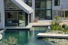 a modern house with a wooden deck and a natural-looking swimming pool with rock borders, it’s a lovely space to enjoy cool water