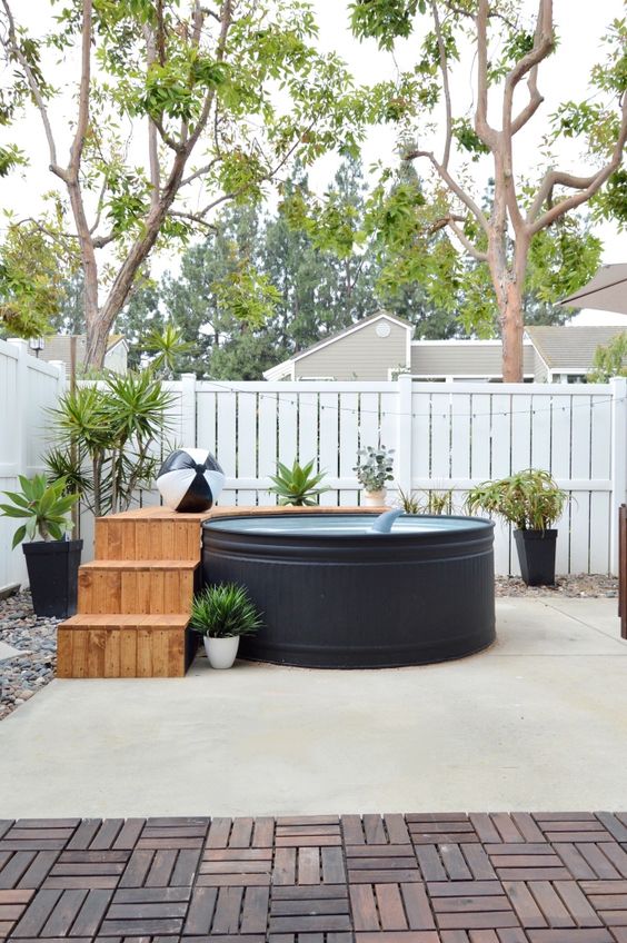a modern outdoor space with a black stock tank pool, a wooden deck, potted plants and lights - who needs more