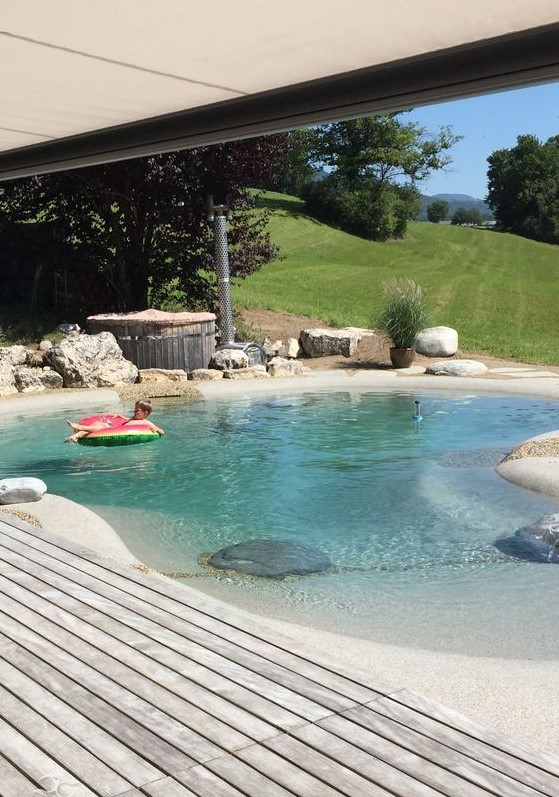 A natural looking swimming pond with rocks around and a wooden deck is a cool solution if you love natural landscaping