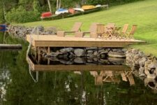 a natural swimming pond clad with rocks, with a large wooden deck and wooden loungers over the pond is cool