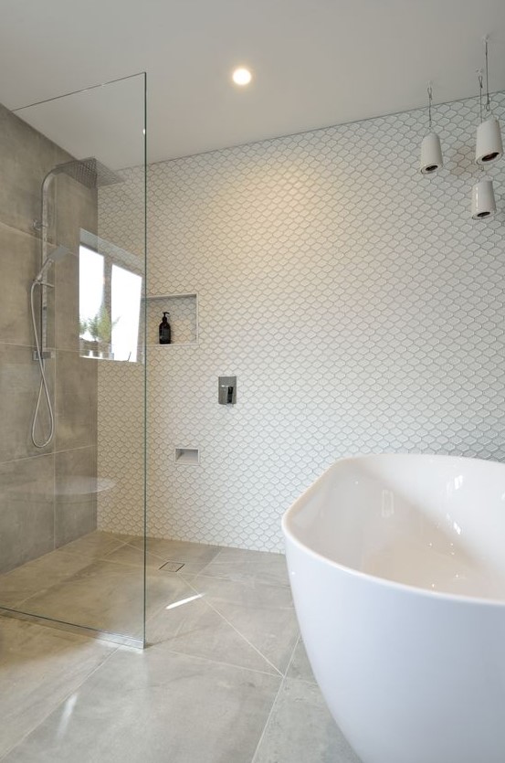 a neutral bathroom with mismatching tiles, an oval tub, a grey tile accent wall, pendant porcelain pendant lamps