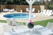 a neutral contemporary space with loungers and white garden furniture and a round pool clad in white, too