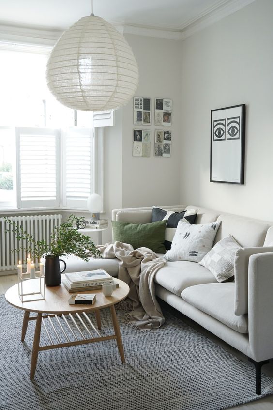 a neutral living room with a creamy sofa and printed and green pillows, a large rug, a gallery wall, a coffee table and some greenery