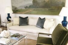 a neutral living room with a creamy sofa, elegant green chairs, an acrylic table, side tables with lamps and an oversized artwork