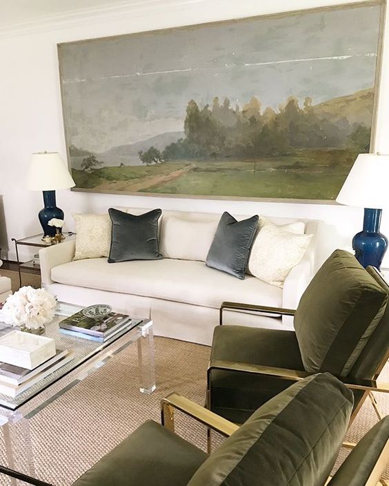 a neutral living room with a creamy sofa, elegant green chairs, an acrylic table, side tables with lamps and an oversized artwork