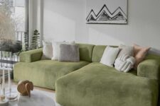 a neutral living room with a low green sofa and neutral pillows, a coffee table with some decor, a neutral rug and a fun artwork