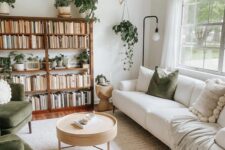 a neutral living room with a stained bookshelf, a creamy sofa, green chairs and pillows and lots of potted plants
