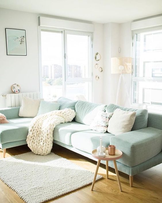 a pastel living room with a light green sectional, a side table, lots of pillows and a blanket and some cool decor