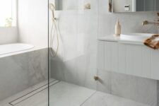 a serene minimalist bathroom with grey large scale tiles, a tub clad with tiles, a shower space, a vanity and brass touches