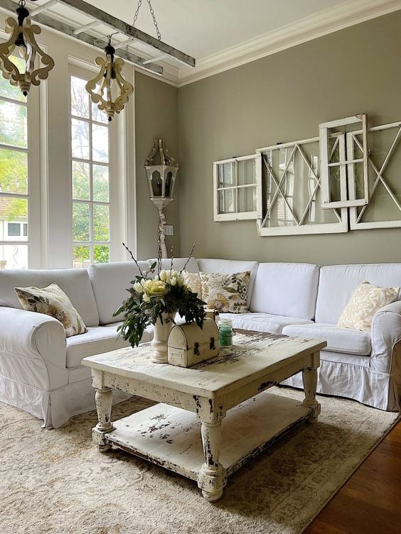 a shabby chic living room with grass green walls, a white corner sofa, a shabby chic coffee table, some window frames and pendant lamps