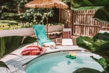 a stock tank pool, a wooden bench, loungers and pillows, floats and greenery around, an umbrella is cool