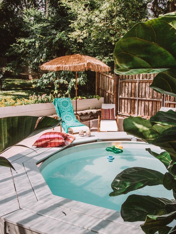 a stock tank pool, a wooden bench, loungers and pillows, floats and greenery around, an umbrella is cool