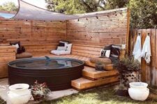 a stylish pool nook with a black stock tank pool, planked screens, wooden ladders and a bench, potted plants and printed pillows