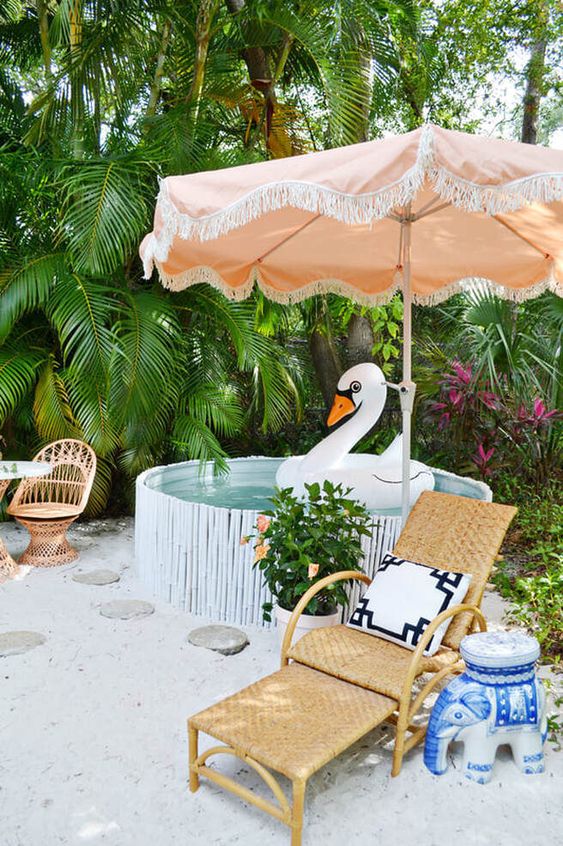 a tropical outdoor space with a stock tank pool with bamboo, rattan chairs and loungers, some bright decor and blooms