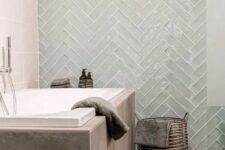 a unique contemporary bathroom clad with taupe tiles and glossy mint chevron ones, with a basket for storage and some neutral textiles