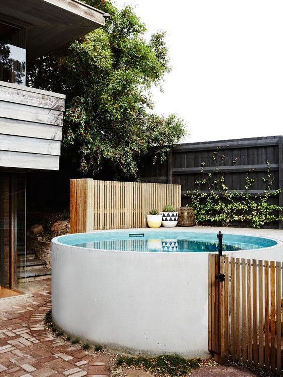 a white stock tank pool with a deck, a wooden fence and some potted plants and greenery around it