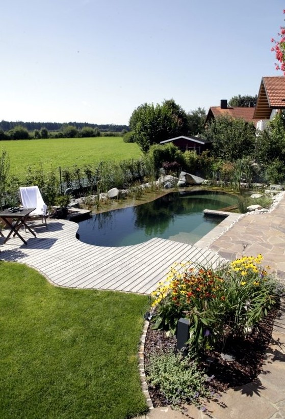 a wooden and stone deck with a small and cool natural swimming pond, just like a plunge pool and greenery