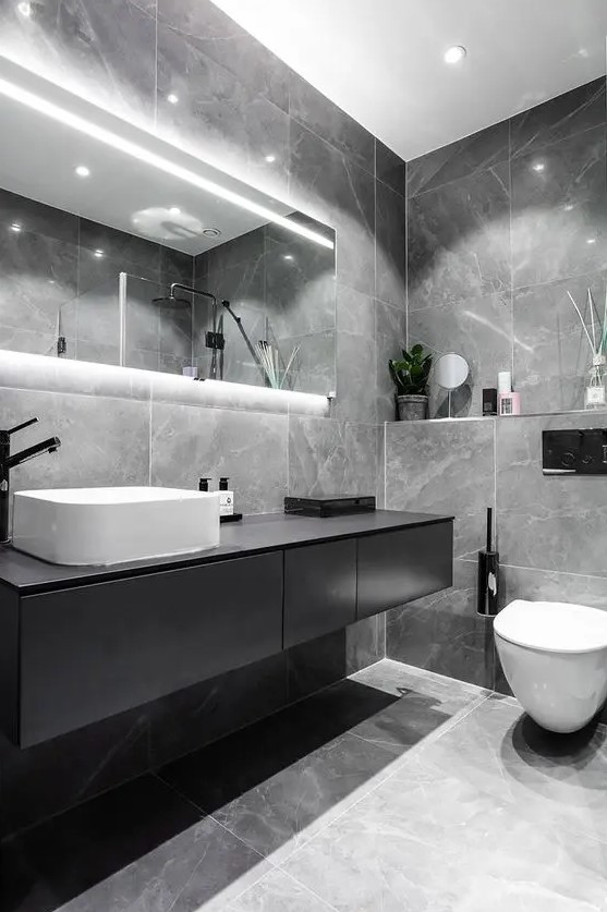 an elegant grey marble tile bathroom, a black floating vanity and a lit up mirror plus white appliances