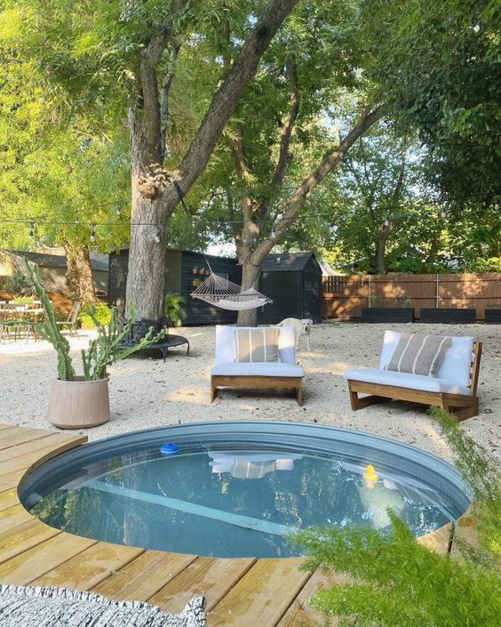 An outdoor space with a gravel yard, seats, an in ground stock tank pool, potted greenery is amazing